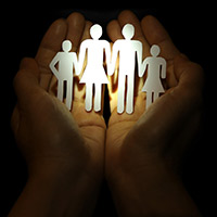 Two upward facing hands holding a paper cut-out of a family of four holding hands.